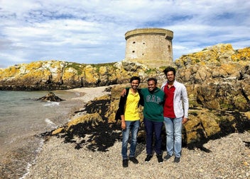 Three visitors standing on a rocky beach beneath a historic Martello Tower