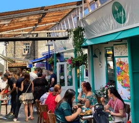 People standing and sitting outside a colourful café on the street