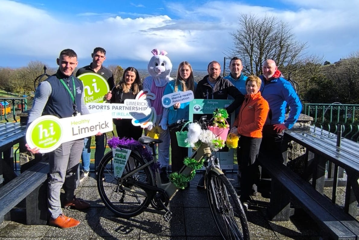 A group of people outdoors with a bike, a person dressed in white bunny costume and some holding hashtag signs.