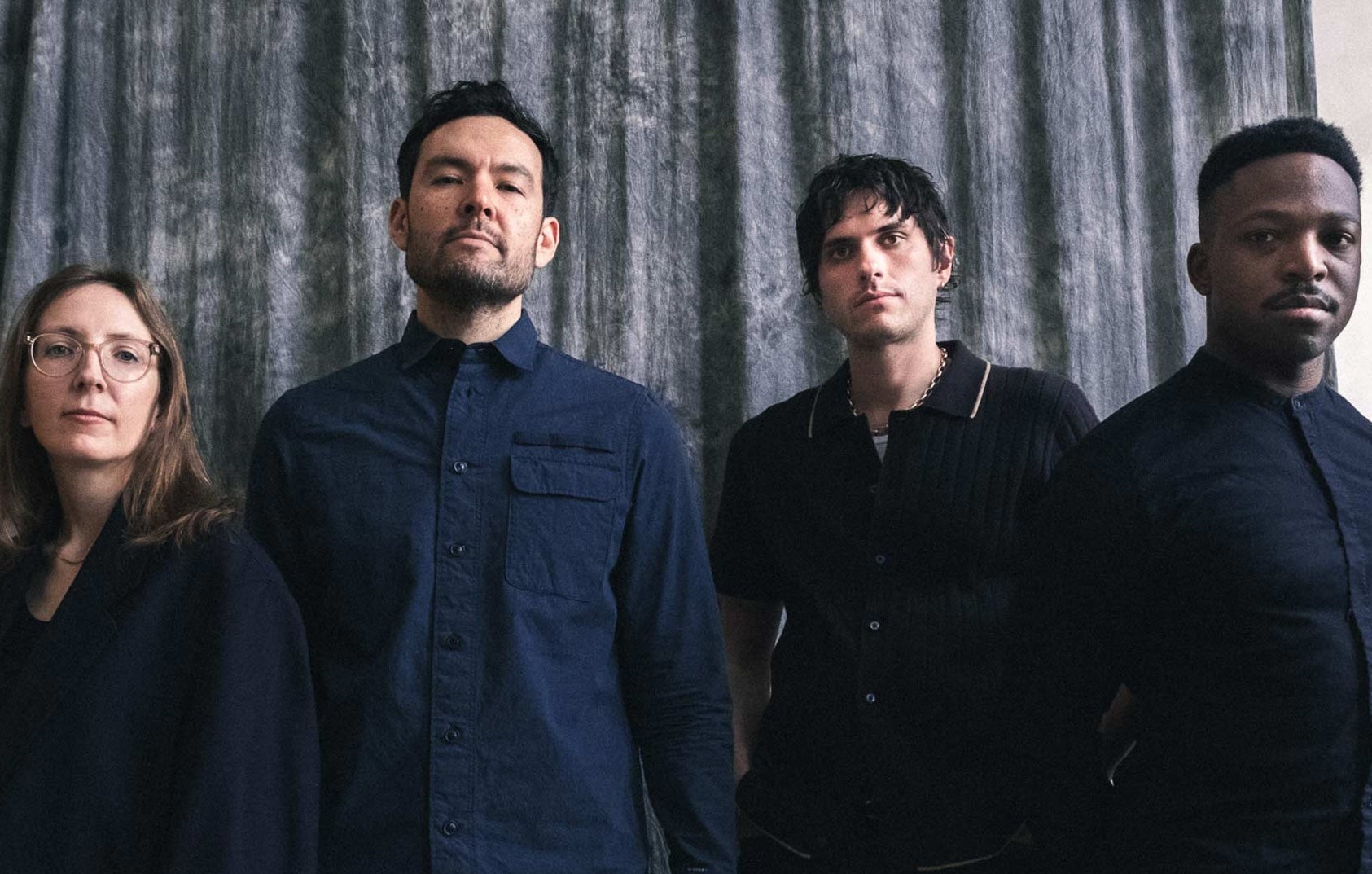 4 serious looking people in a line, dressed in dark clothes.