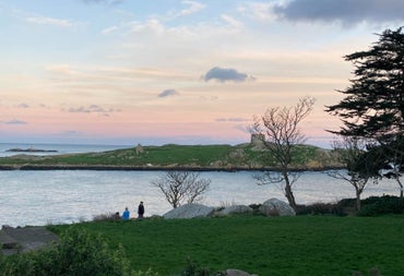 Two people standing in a field next to the sea at sunset