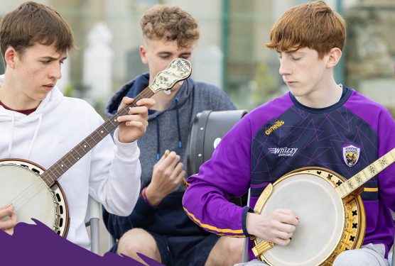 3 young men seated playing musical instruments outdoors, all looking down, concentrating.