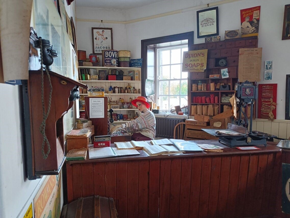 Exhibition with a mannequin behind a desk with books and posters and shelves in the background
