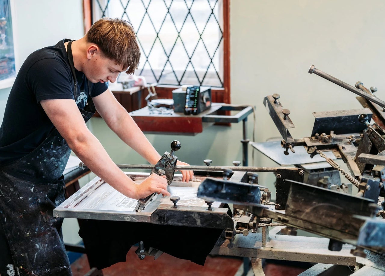 A person working at a screen printing station using a large manual press in a workshop
