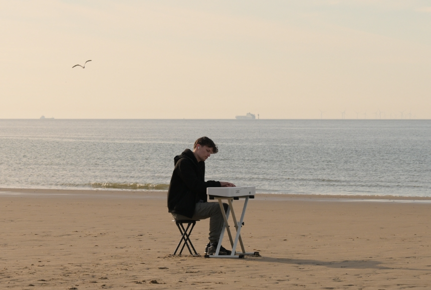 James Malikey - Lost Within The Aether, a man seated at a small portable keyboard on an empty beach