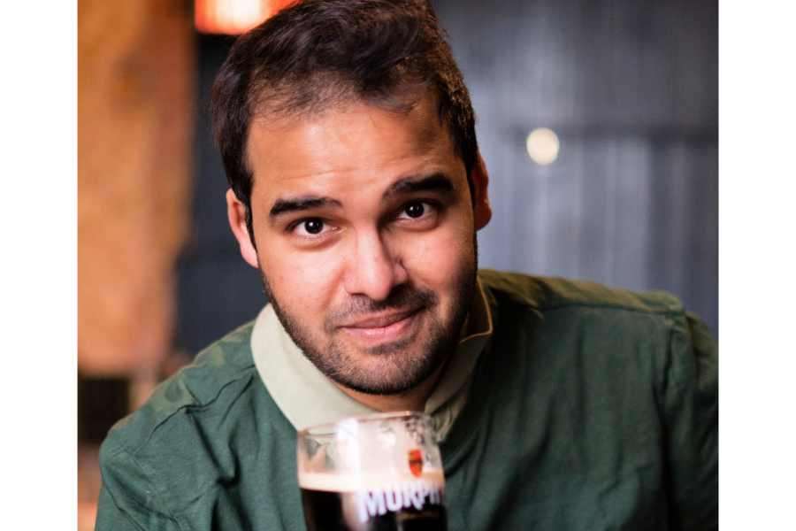 A gently smiling man holding up a pint of stout