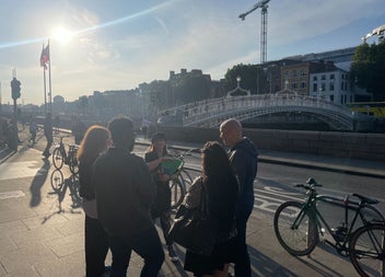 A group gathered beside a bridge on a sunny day taking part in a walking tour along the River Liffey