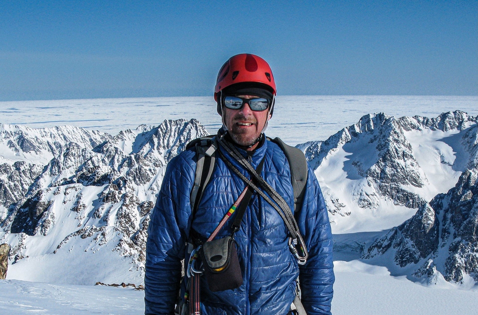 A man in mountaineering gear including helmet and sunglasses on snowy mountain