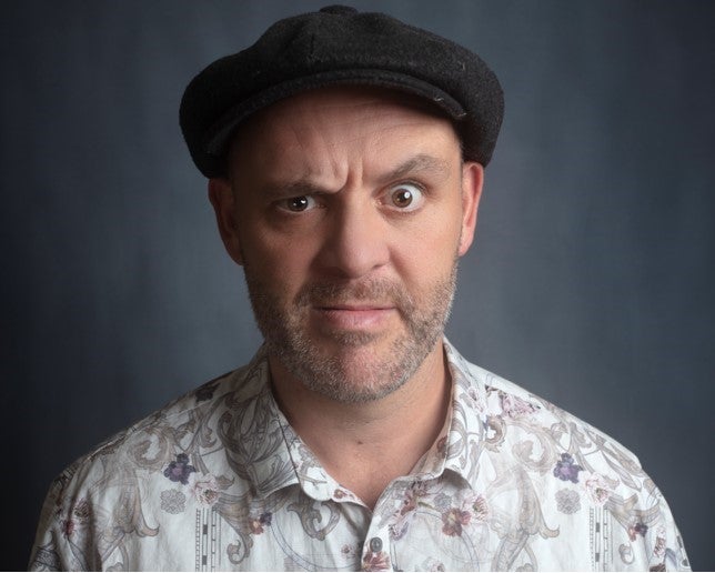 A confused looking man wearing a flat cap and patterned shirt.