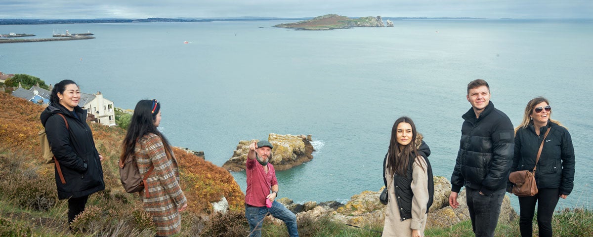 A guide with a group on Howth Cliffs with the sea in the background