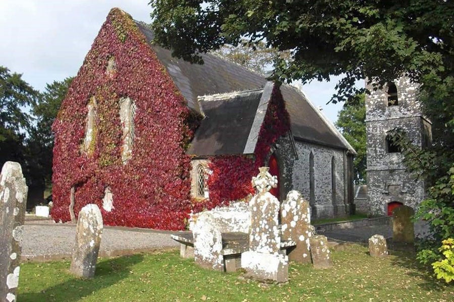 View of the ivy covered gable of the church with headstones visible in the forefront