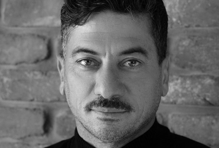 Black and white headshot of man with moustache with slight smile.