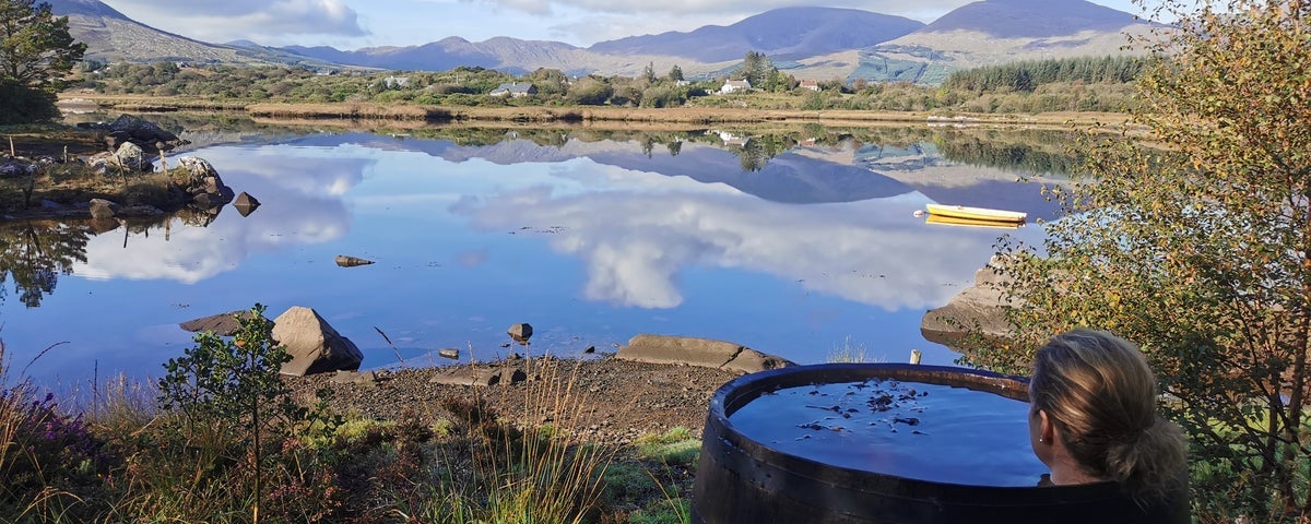 A woman relaxes in a seaweed bath looking out over a lake