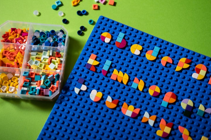 The alphabet made in multi coloured LEGO on a blue board with a box of pieces next to it.