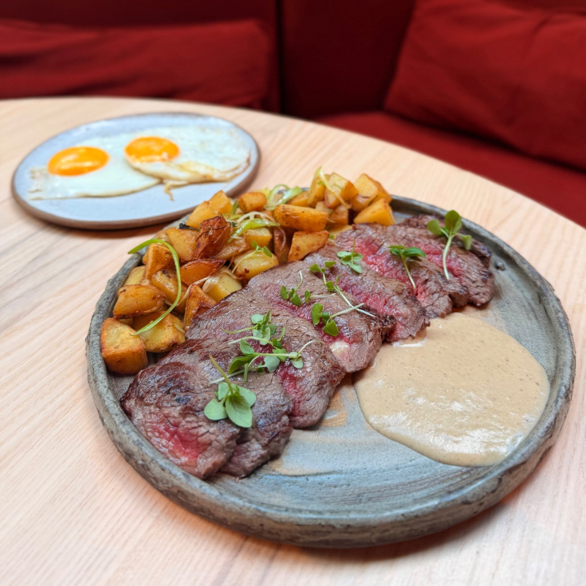 A plated steak dish with roasted potatoes and a creamy sauce with two fried eggs on a side plate