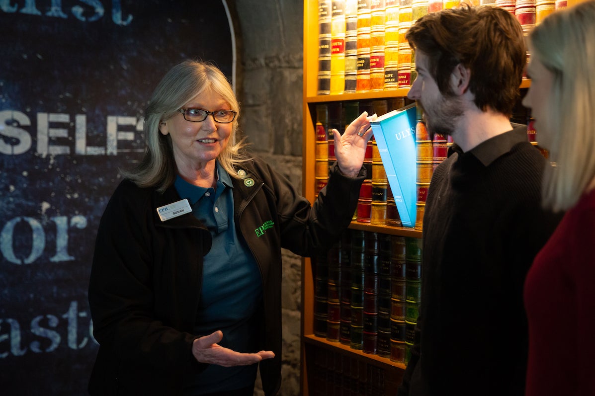 A tour guide is talking to 2 people standing beside an exhibit.