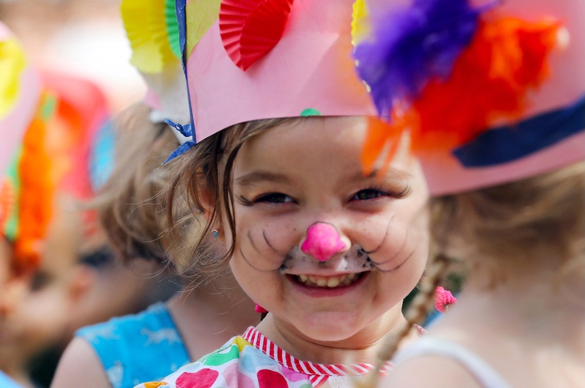A very young smiling girl wearing a hand made pink crown and face painted.