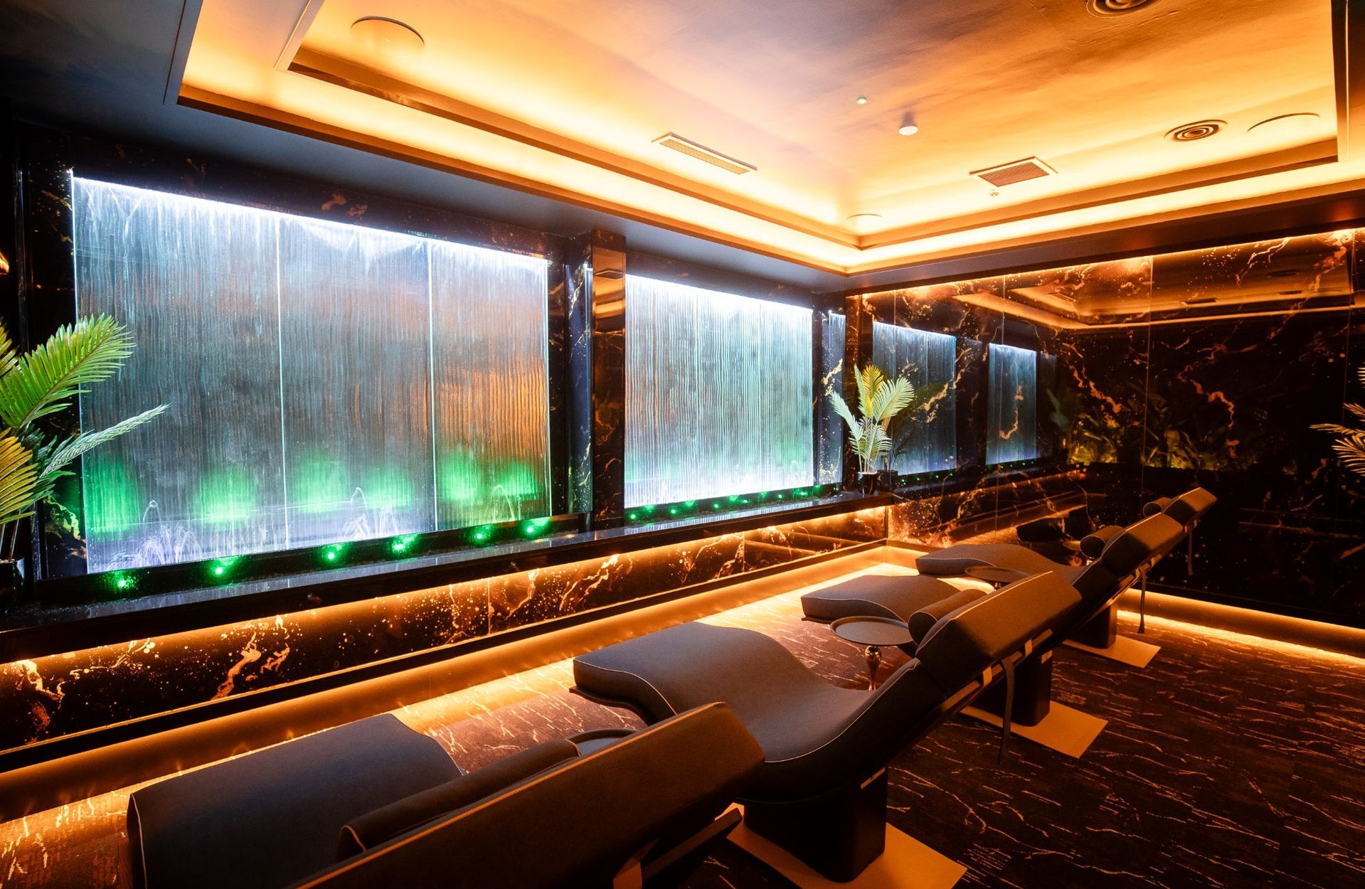 Four comfortable lounge seats in a spa facing a wall with a water feature