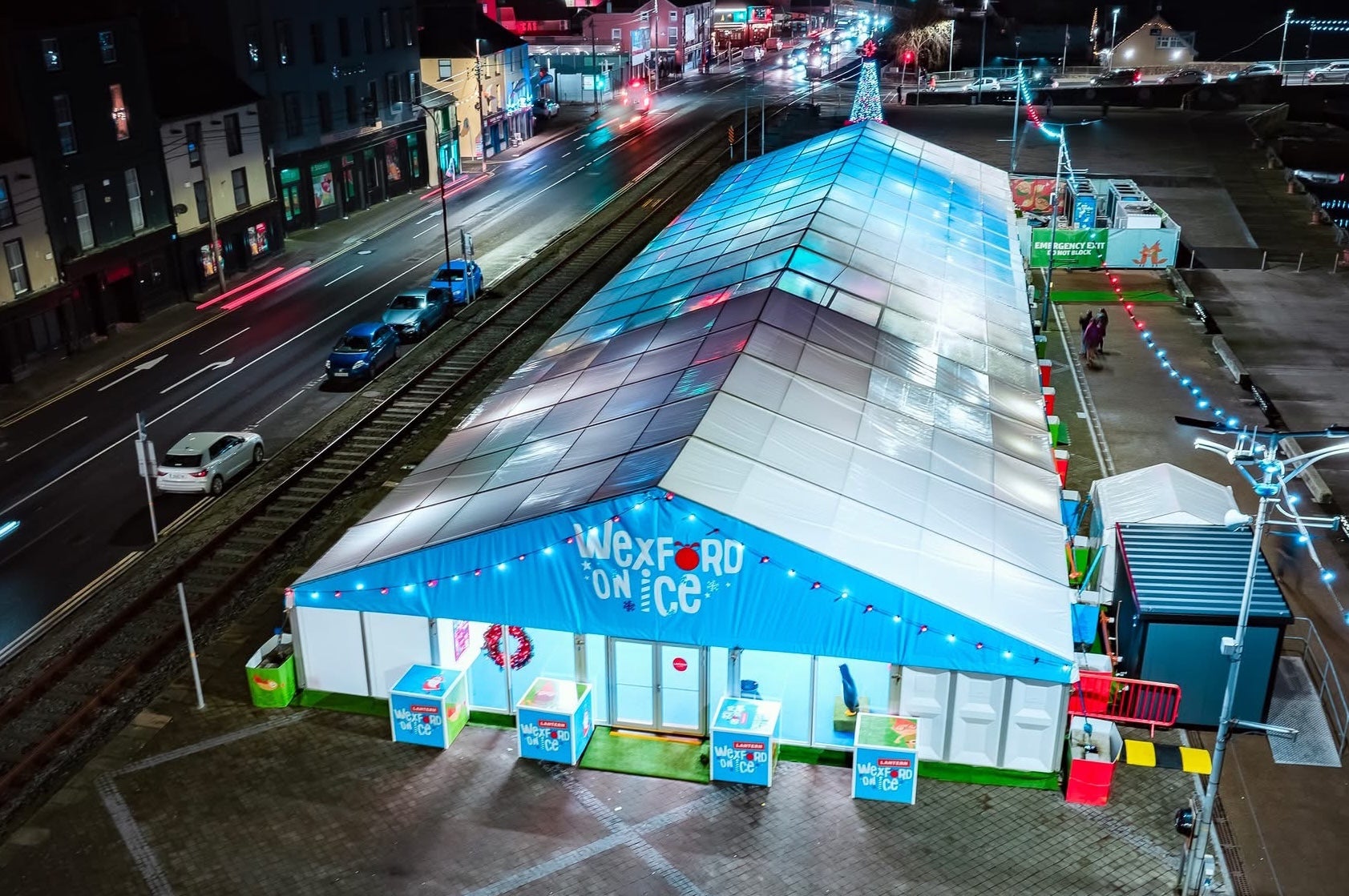 A large tent by a road in a town, lit up a night in white and blue