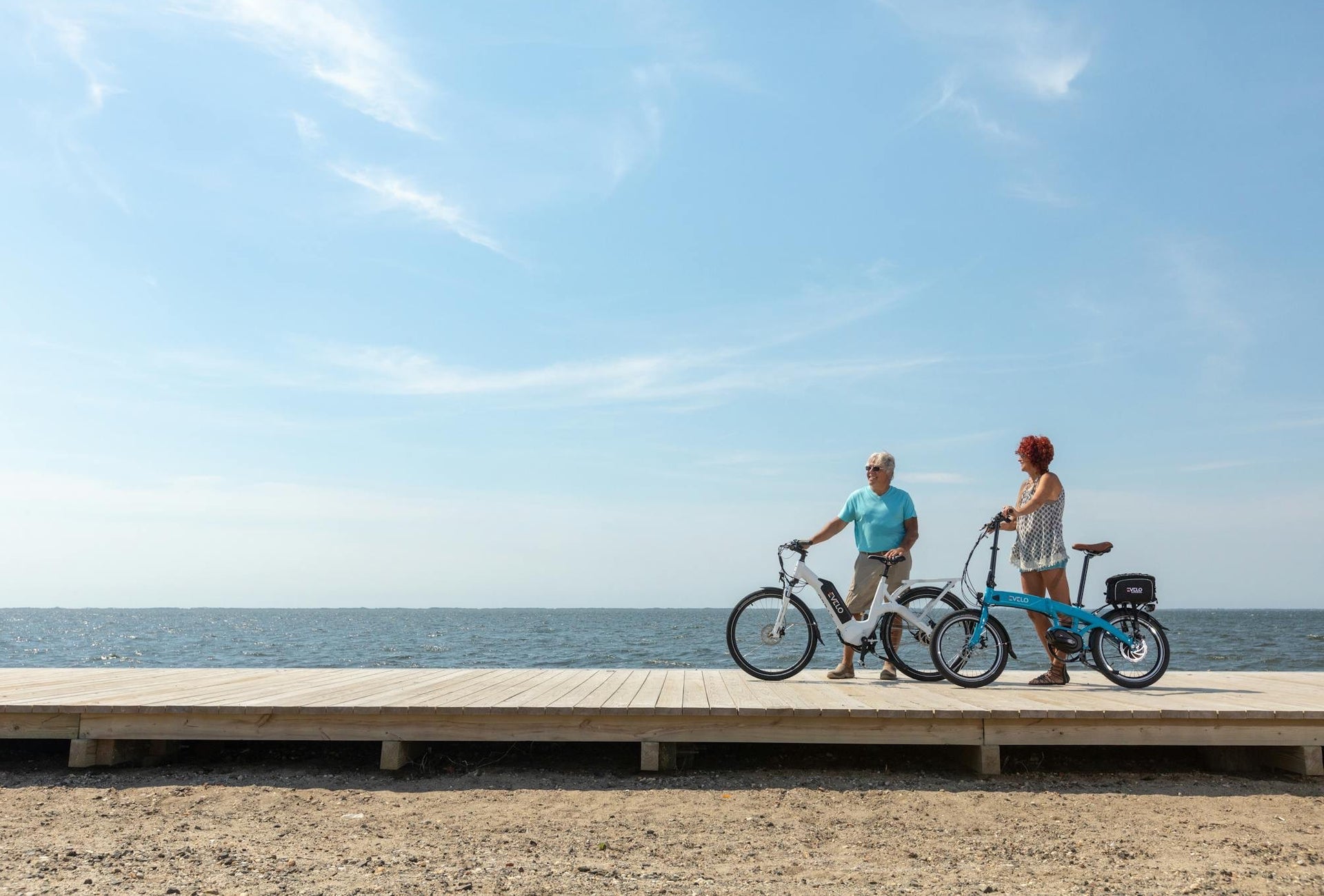 Two people with bikes on a boardwalk on a beach on a sunny day