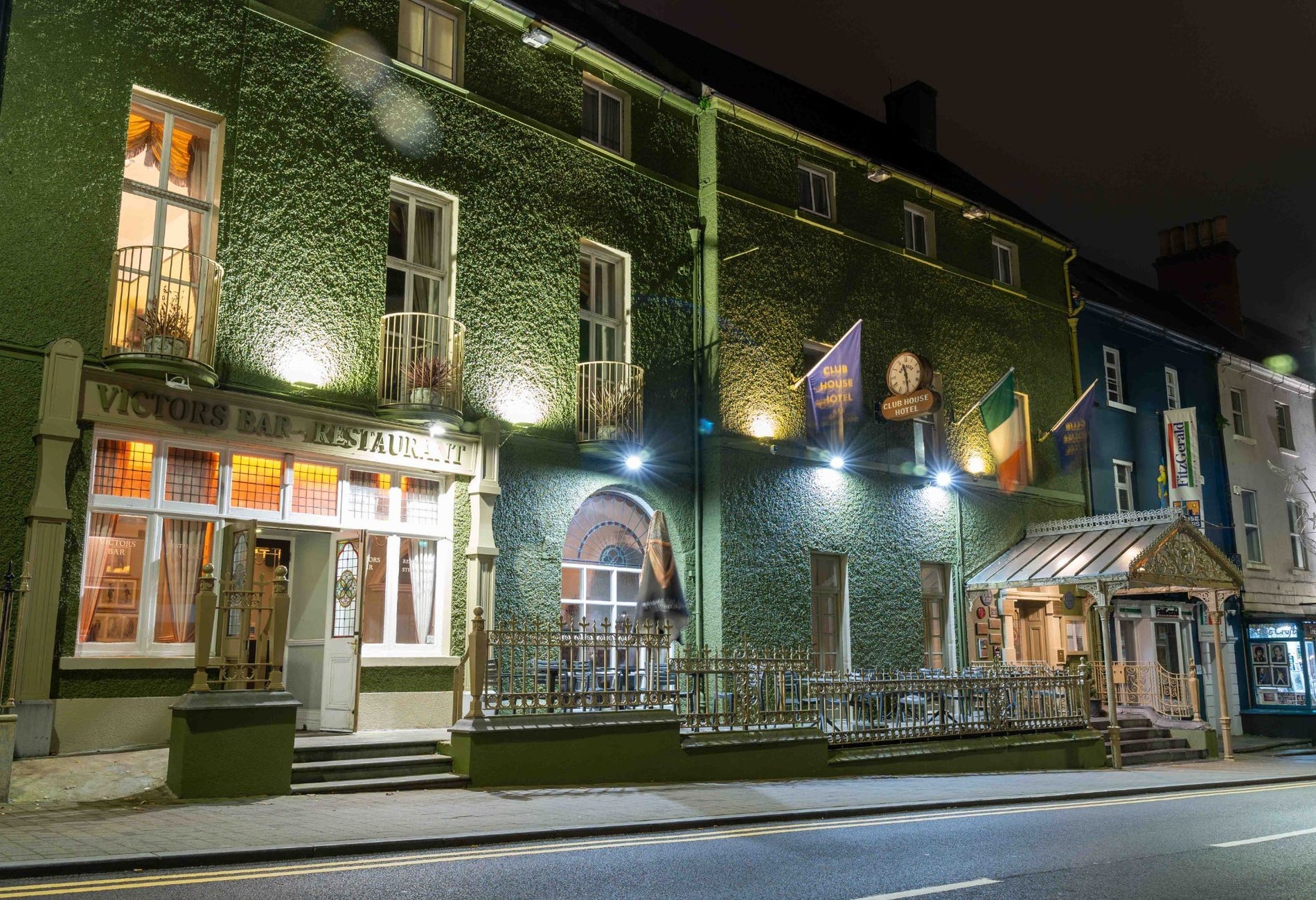 Exterior of a restaurant covered in ivy with flags on display and railings in front