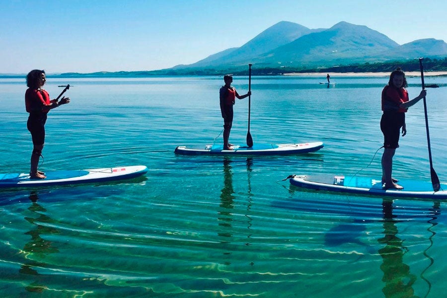 Three girls SUPing on the sea with mountains in the background