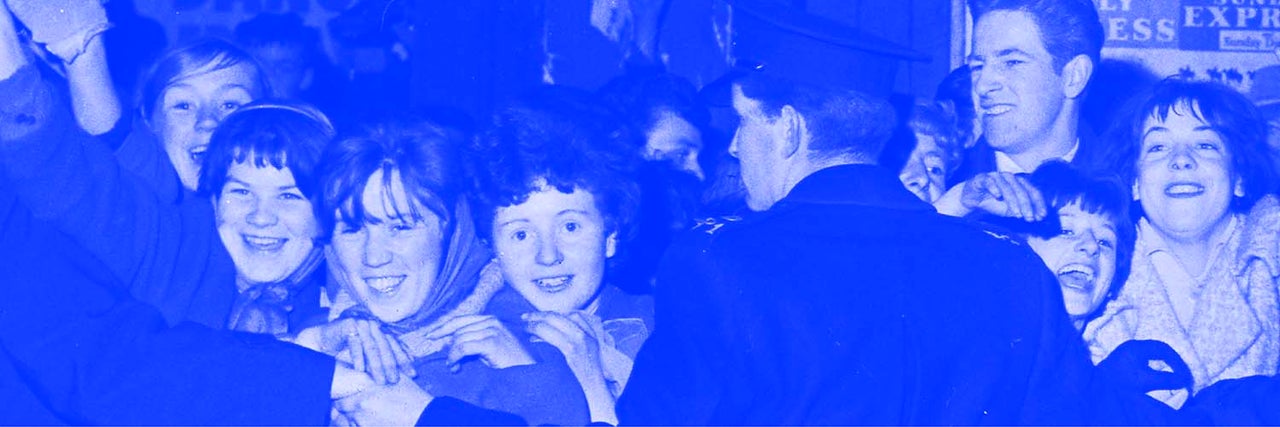 Blue and grey photo from 60s of happy young women waiting for an idol being held back by line of men