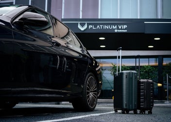 A black car parked outside a building with two upright suitcases placed beside it