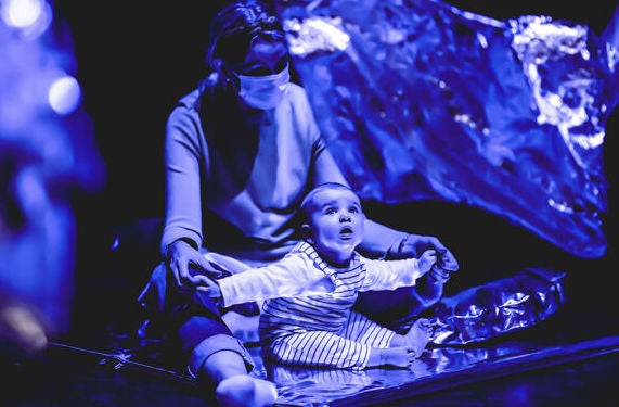 A baby is seated on lap of adult, looking up engaged.