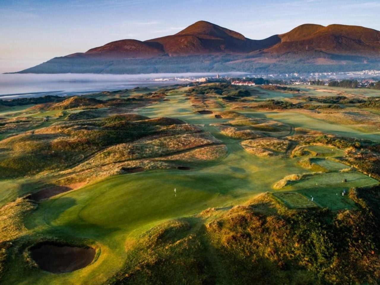 Drone image of a links golf course with mountains in the background