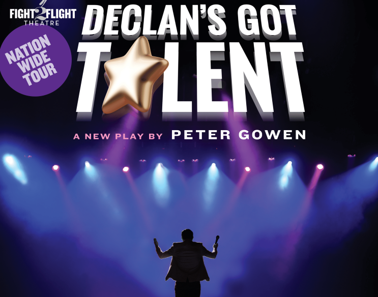 Viewed from the back of a stage, a figure is silhouetted against front of stage with spotlights shining down on it with large white event text above.