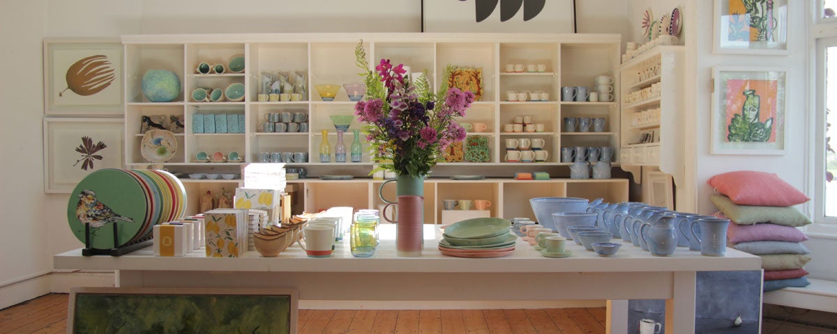 A table with an assortment of pottery with shelves in the background also full of pottery