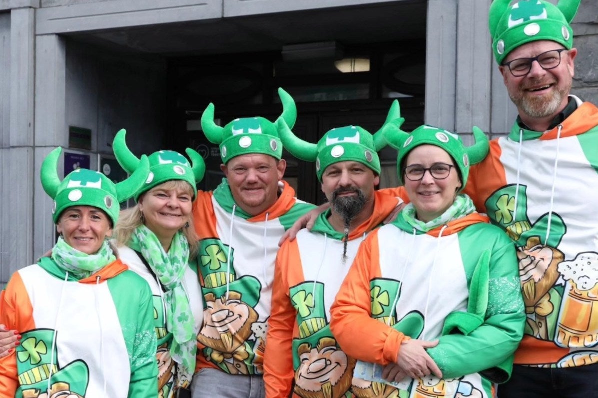 Group of smiling people in green hats with horns and sweatshirts with smiling leprechauns.