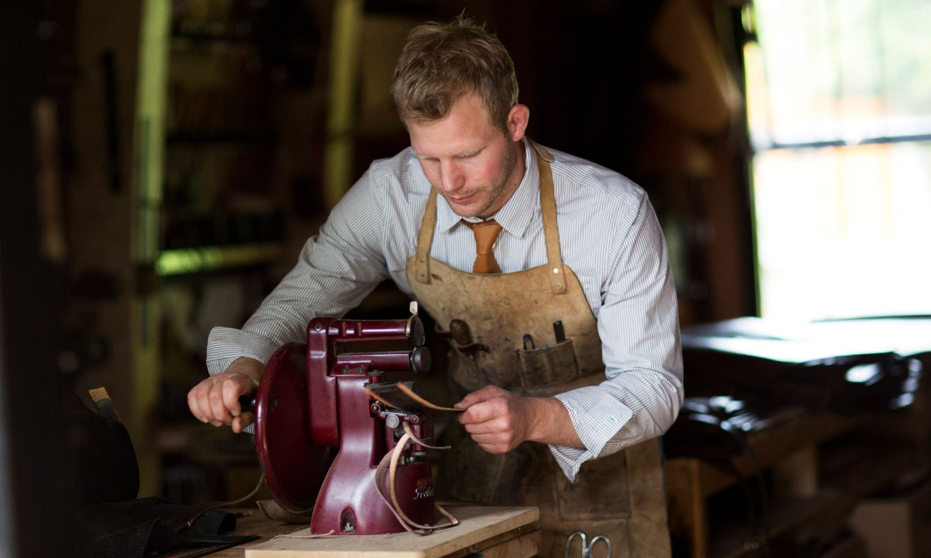 A craftsman in an apron working on a leather bag