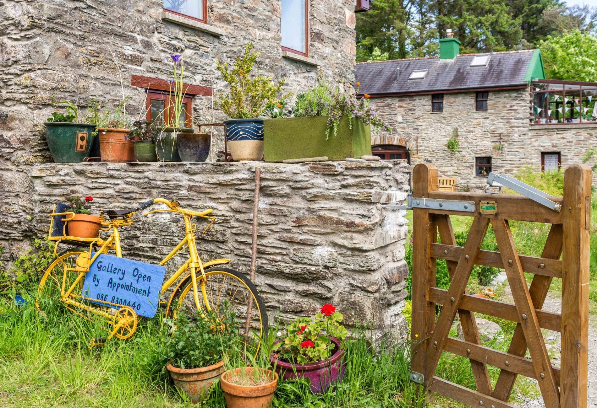 Stone house and wall with a yellow bike resting against it a wooden gate and pots of flowers