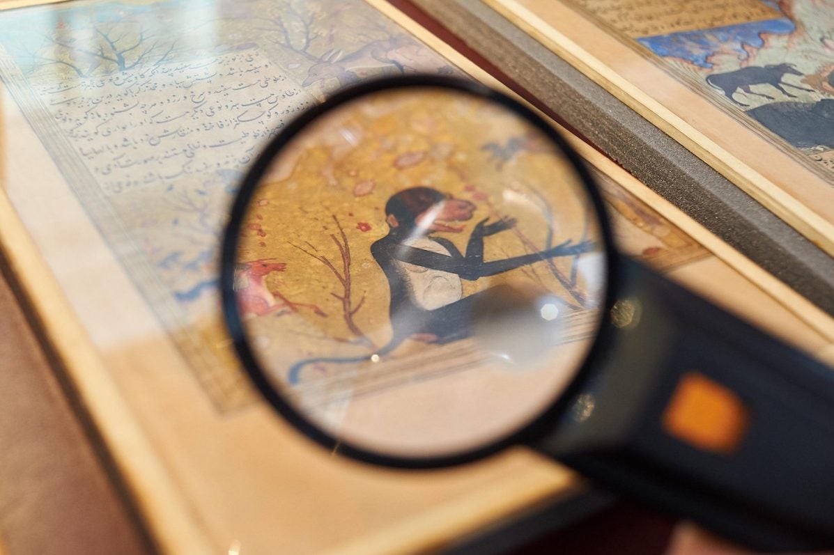 Close up view seen via a black magnifier of an old drawing of a monkey in a book.