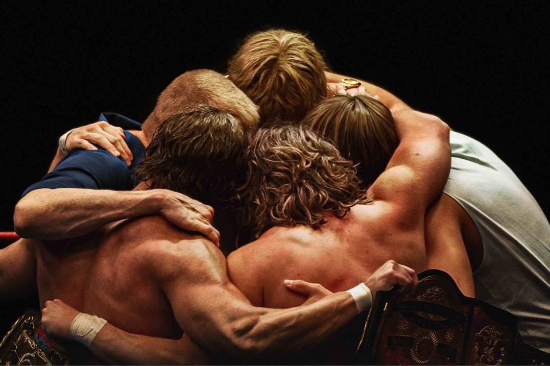 A group of 4 men in a tight huddle in a wrestling ring