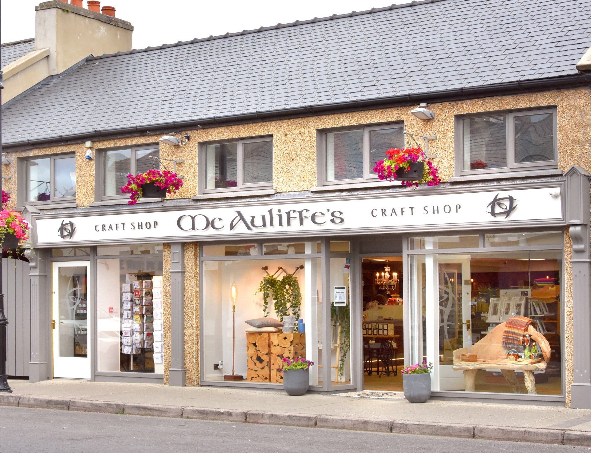 Grey yellow and white shop front with two hanging baskets and two flower pots at the entrance