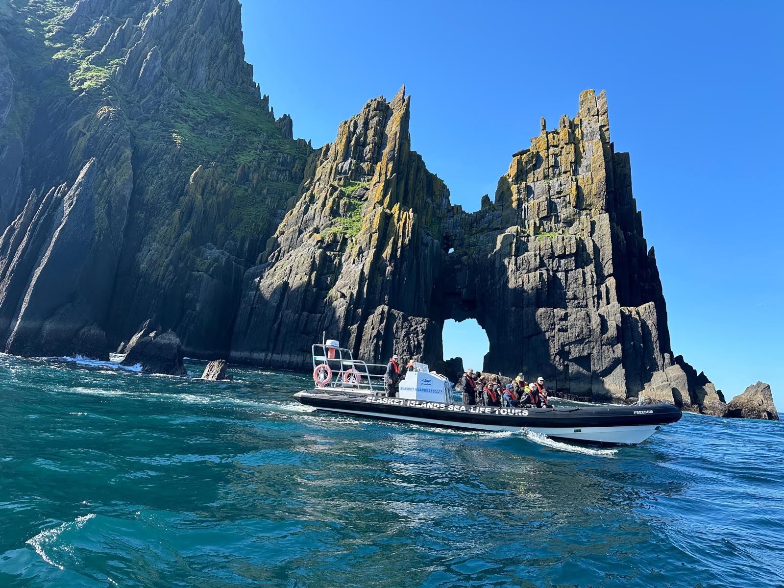 A group of people in a boat in front of a sea arch