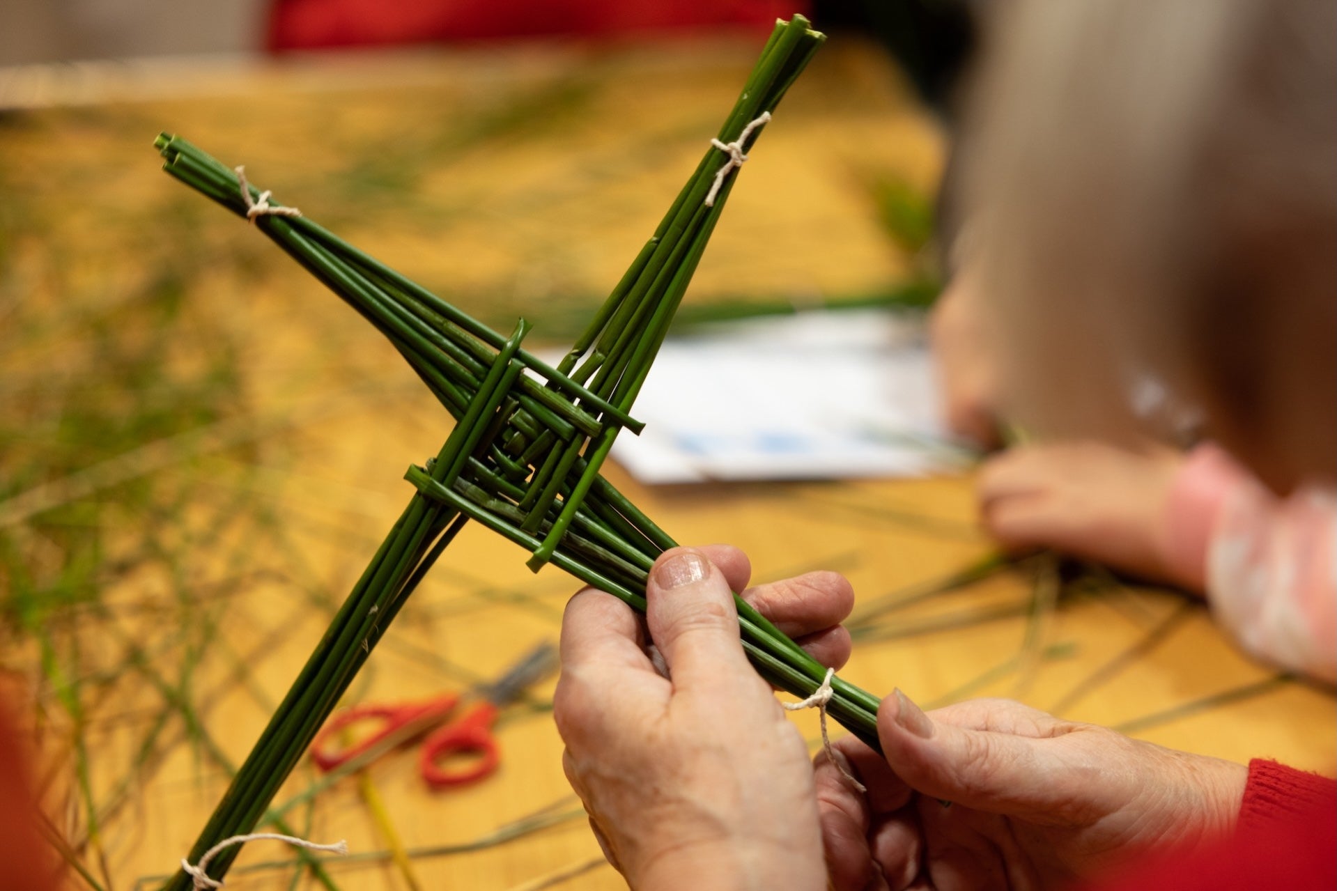 A close of up view of pair of hands holding a green 4 pronged cross