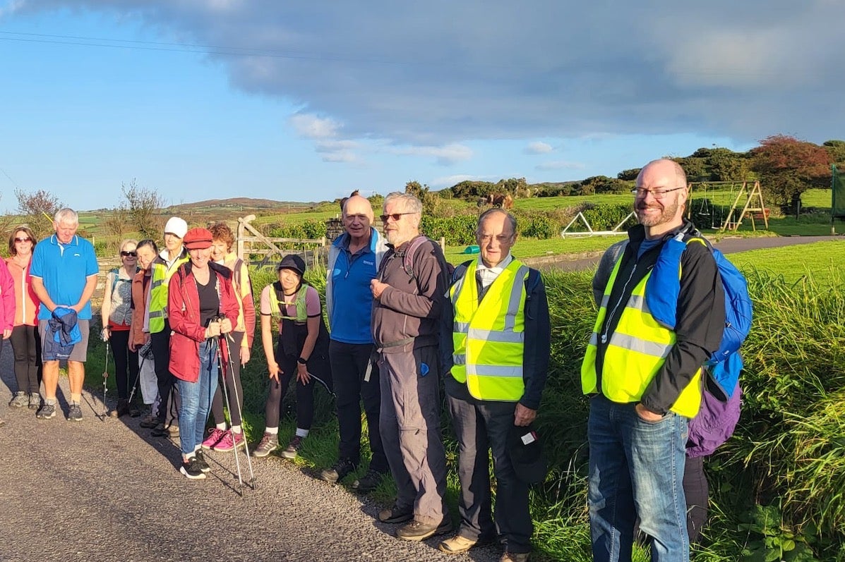 A group photo of people gathered by the edge of a country road, some wearing Hi Vis jackets.