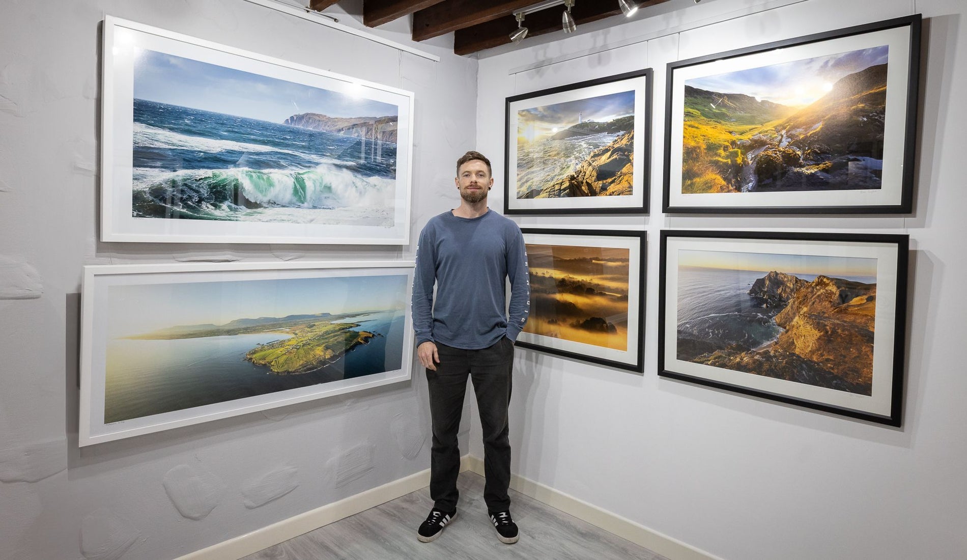 A wall with six large framed photographs and a man standing in front of them