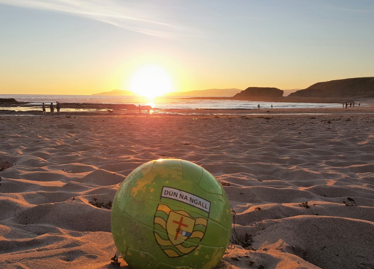 A view of a football sitting on a sandy beach at sunset