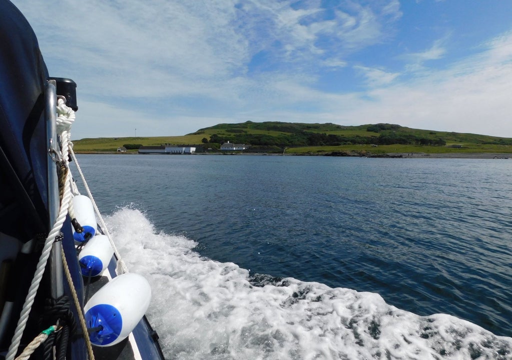View from the side of a rib style boat travelling across the sea towards an island