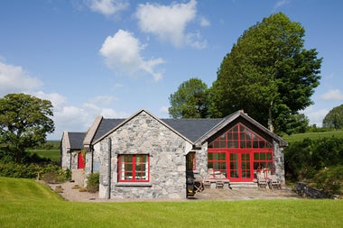 A house with stone walls and large red windows overlooking a garden