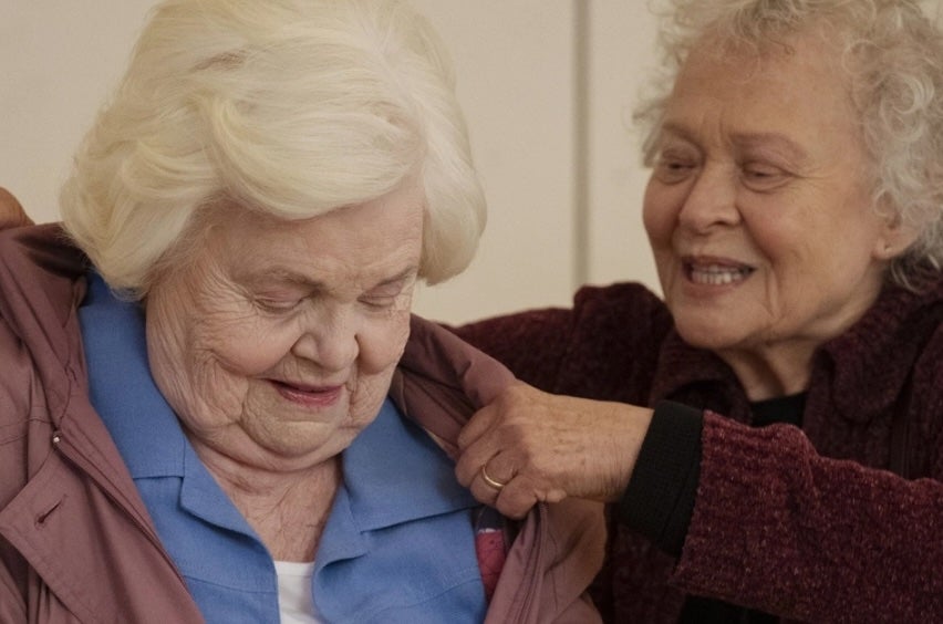 An old woman is helping another old woman put her coat on.