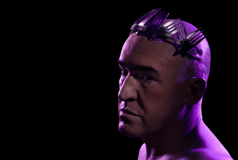 Headshot of very sad looking man with no hair and a crown of fork heads, darkly lit with purple hues.