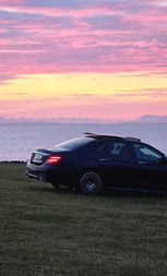 A luxury car parked at the coast with a sunset view
