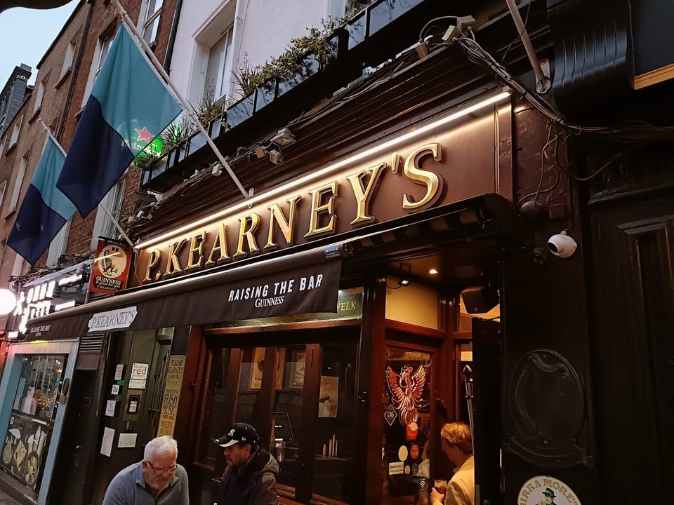 Outside of pub at dusk with two flags above a sign that reads P Kearneys