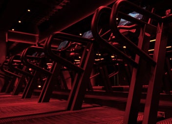 A dark red lit treadmill studio with rows of high performance machines